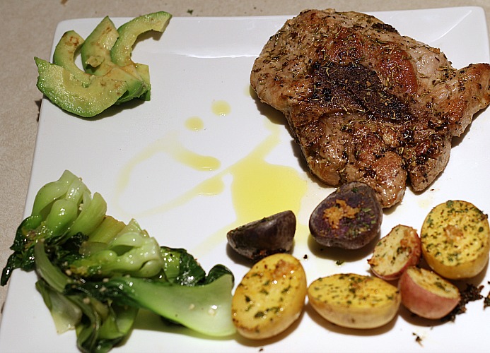Garlic Butter Pork Chop Served with avocado, oven roasted baby potatoes, and baby bok choy