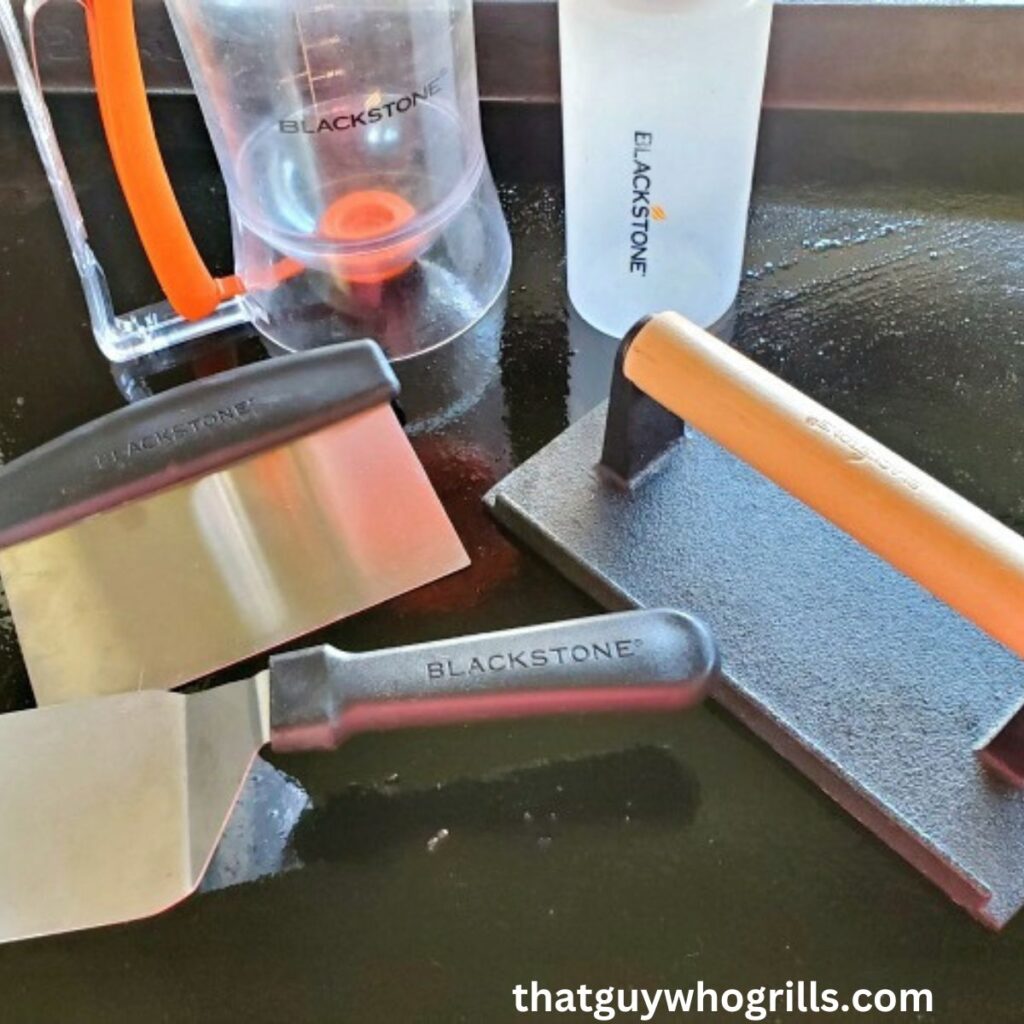 Blackstone Spatula, Scraper, pancake dispensor, and squeeze bottle on a griddle with a bacon press