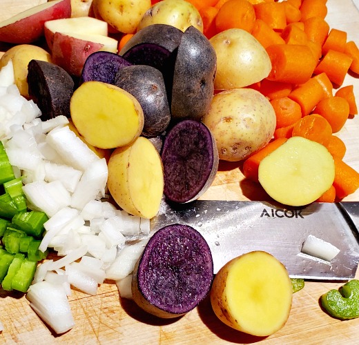 Chopped Baby Potatoes, Baby carrots, white onions, and celery on cutting board with knife