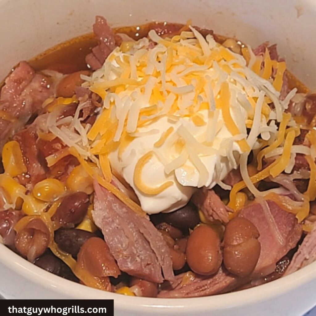 Smoked Pulled Pork Chili Served with Sour Cream and cheese on top in white bowl 