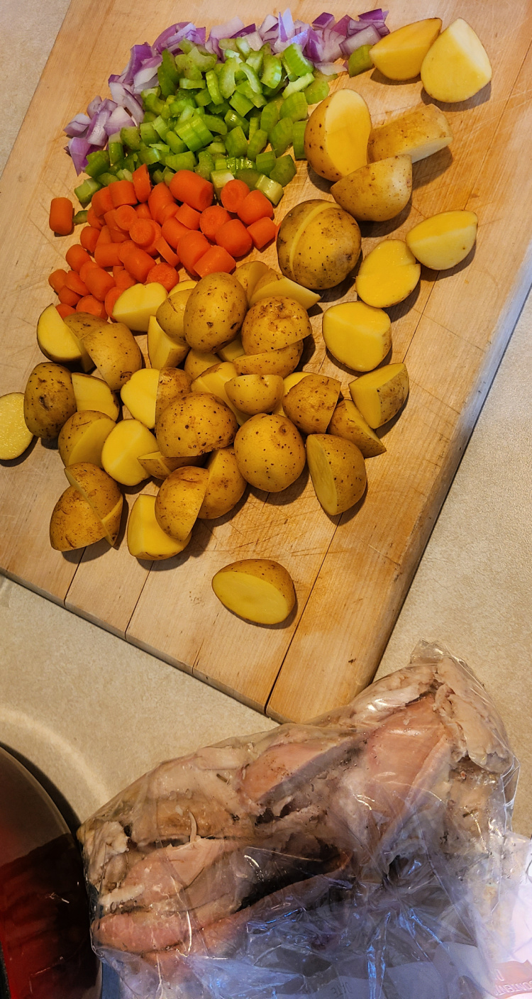 Smoked Turkey in a bag next to cutting board with cut baby carrots, baby potatoes, red onion, and celery 