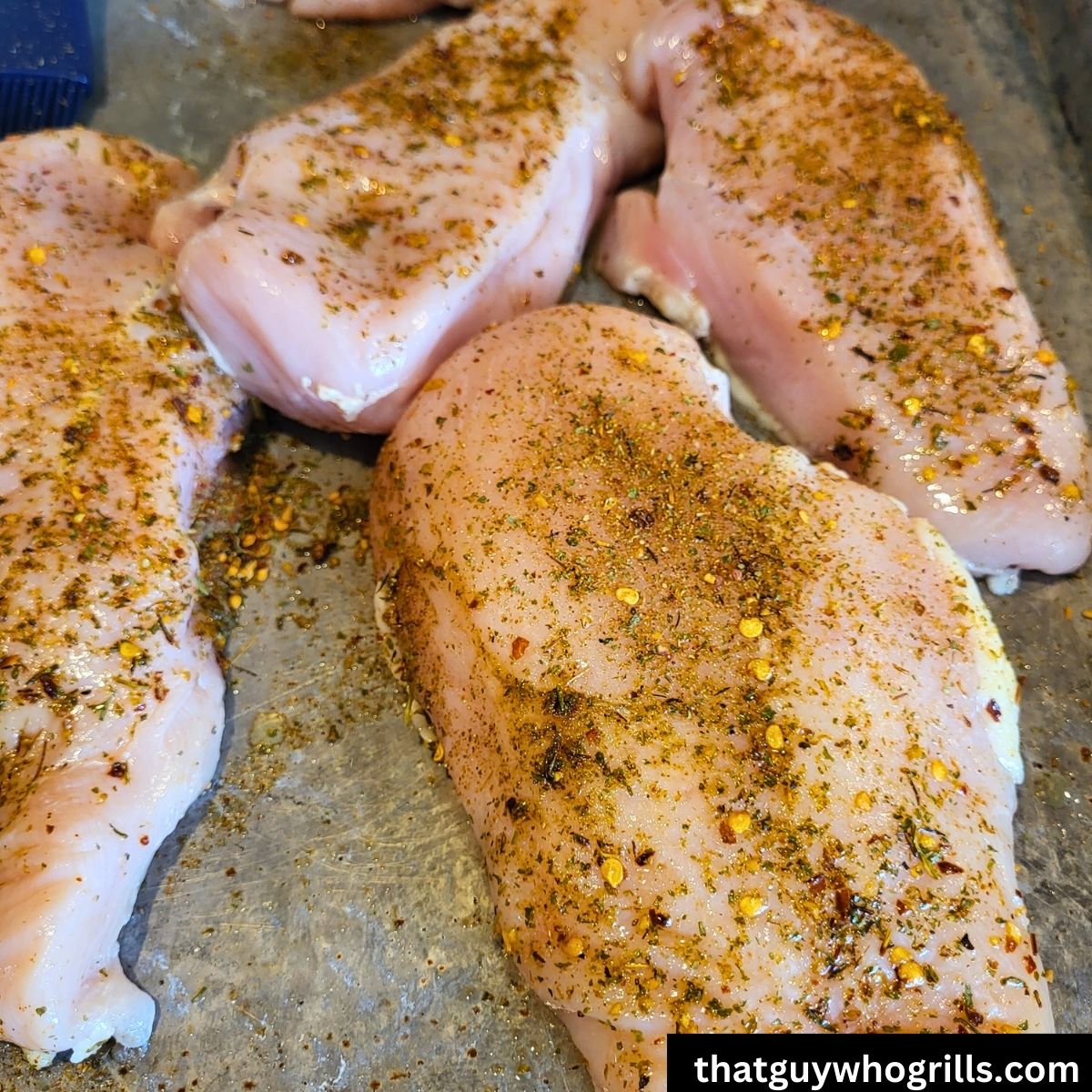 Raw boneless skinless chicken breasts seasoned with seasoning on a cookie sheet
