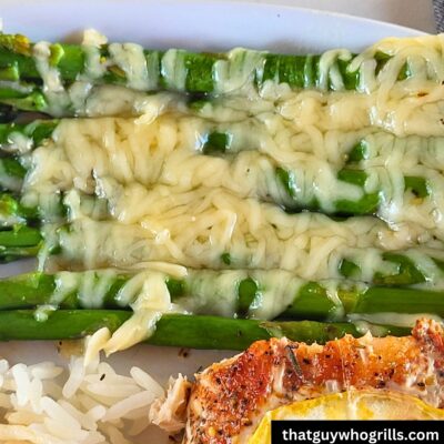 Cheesy Grilled asparagus on a white plate served with grilled salmon and white rice