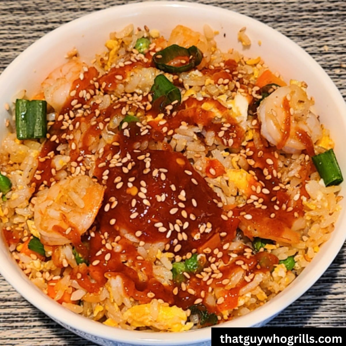 Shrimp fried rice served in bowl topped with sauce and sesame seeds